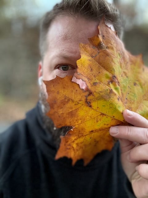 John Paul Davis, holding a large fallen leaf in front of his face, obscuring it.